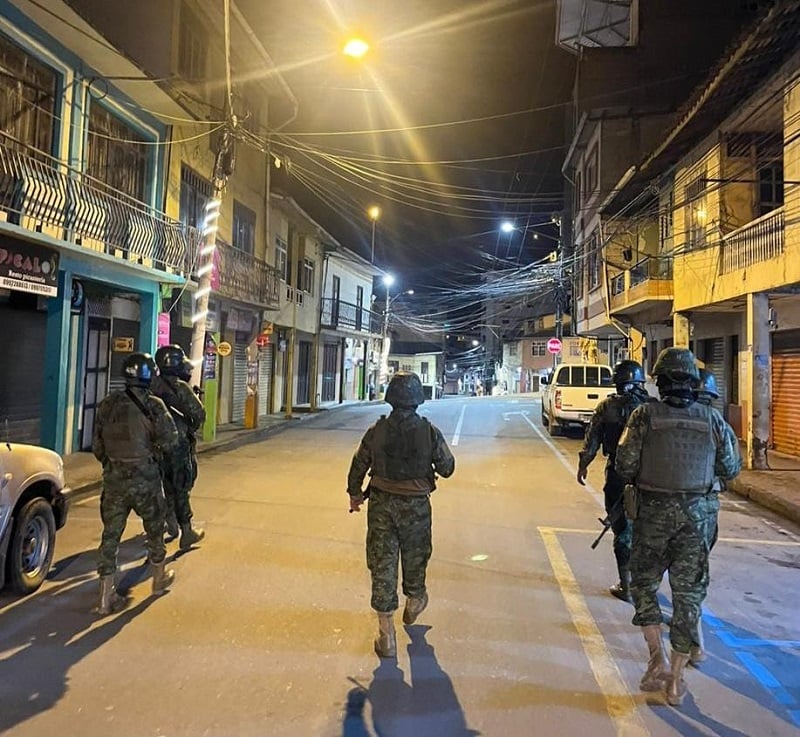 Militares armados patrullan de noche una calle con locales cerrados en una ciudad de la costa ecuatoriana.