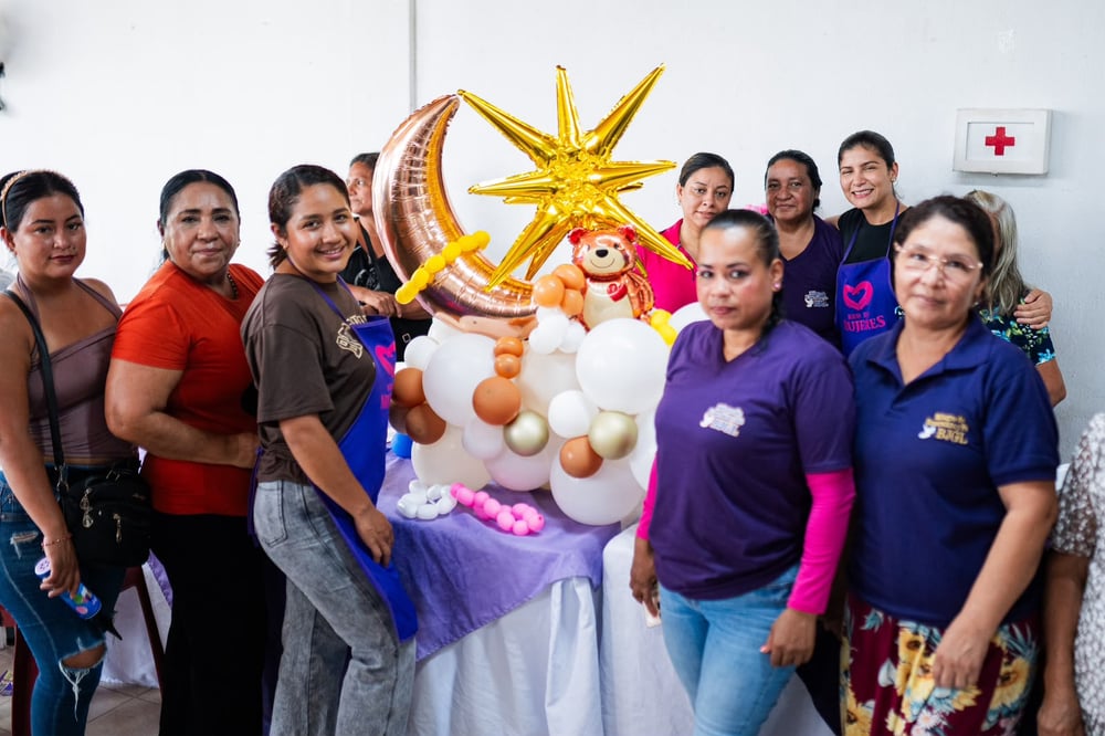 Grupo de mujeres sonrientes posa junto a una decoración de globos con luna, estrella y osito sobre una mesa.