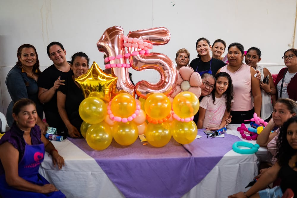 Grupo de mujeres posa junto a globos dorados y número 15 en un taller de la Red de Mujeres.
